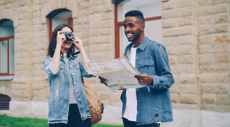 Two smiling tourists with a map and camera exploring a city street in daylight. — 10 Innovative Online Travel Websites