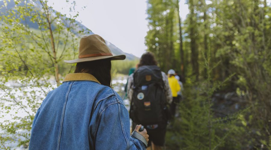 A group of hikers walking through a scenic forest trail by a river in the daytime. — Best Adventure Holidays of 2016 To Fill