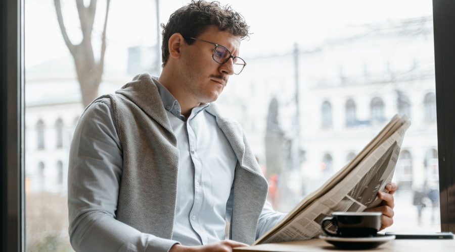 Adult man reads a newspaper by a café window, enjoying a coffee break indoors. — Exploring the Costs of Breast Implants in Mi