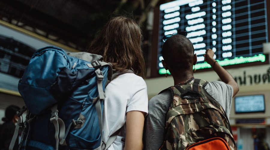 Two backpackers checking the digital board at a train station for travel information. — Guide to preparing yourself for the f