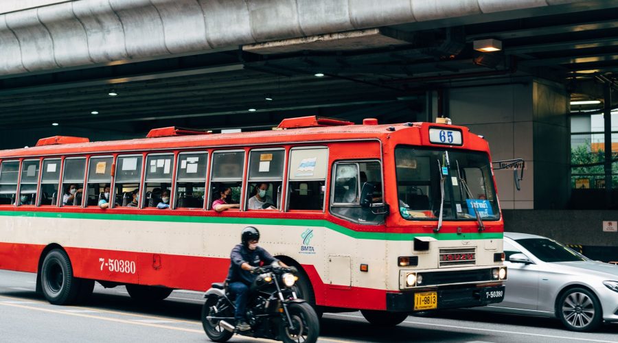 A busy street scene in Bangkok featuring a red bus, motorcycle, and car under an overpass. — Local Taxi Services: A Comprehen