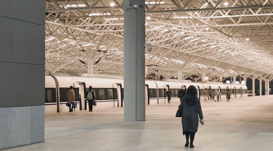 A modern train station interior with passengers walking towards a waiting train. — The Best Beaches in Pondicherry: A Guide t