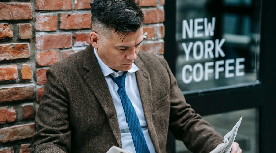 Man in formal attire reading a newspaper outside New York coffee shop. — Winning Games and Big Jackpots at Live Casino Online